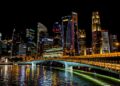 Stunning Singapore cityscape featuring vibrant skyscrapers, illuminated bridge, and reflections over the river at night.