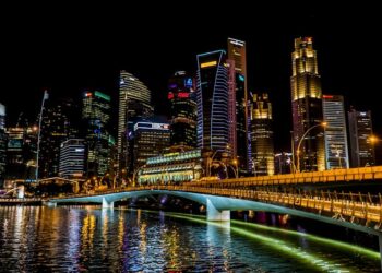Stunning Singapore cityscape featuring vibrant skyscrapers, illuminated bridge, and reflections over the river at night.