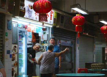 People at a brightly lit street food stall with lanterns