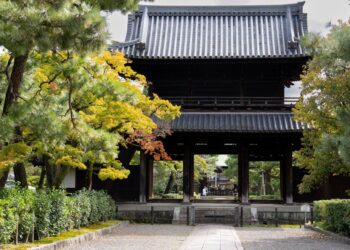 Authentic Japanese temple gate framed by vibrant autumn foliage, showcasing cultural heritage.
