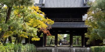 Authentic Japanese temple gate framed by vibrant autumn foliage, showcasing cultural heritage.