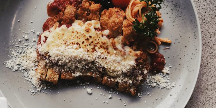 Crispy chicken parmigiana topped with cheese and tomato, served with spaghetti on a plate.
