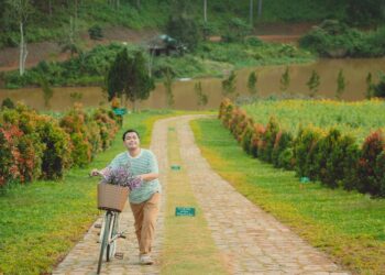 A man strolling with a bicycle filled with flowers along a scenic path in Dalat, Vietnam.
