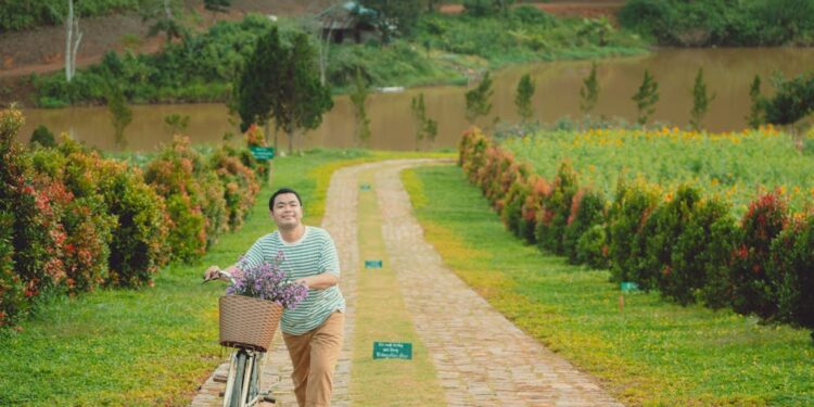 A man strolling with a bicycle filled with flowers along a scenic path in Dalat, Vietnam.