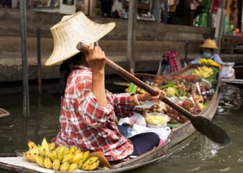 Woman paddling boat at a vibrant floating market in Bangkok, Thailand.