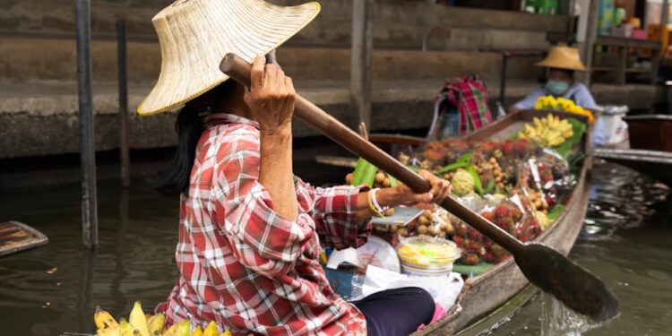 Woman paddling boat at a vibrant floating market in Bangkok, Thailand.
