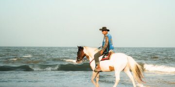 A man rides a horse along the beach in Thailand at sunrise, showcasing serene ocean views.