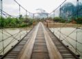 Wooden suspension bridge over river with misty mountains in Vang Vieng, Laos.