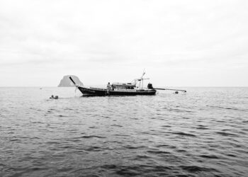 Black and white photo of a longtail boat in calm waters, showcasing serene travel and nature vibes.