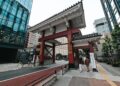 Street view of a traditional Japanese gate amidst modern Tokyo architecture.