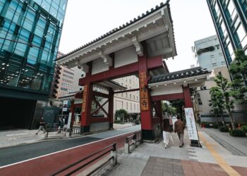 Street view of a traditional Japanese gate amidst modern Tokyo architecture.