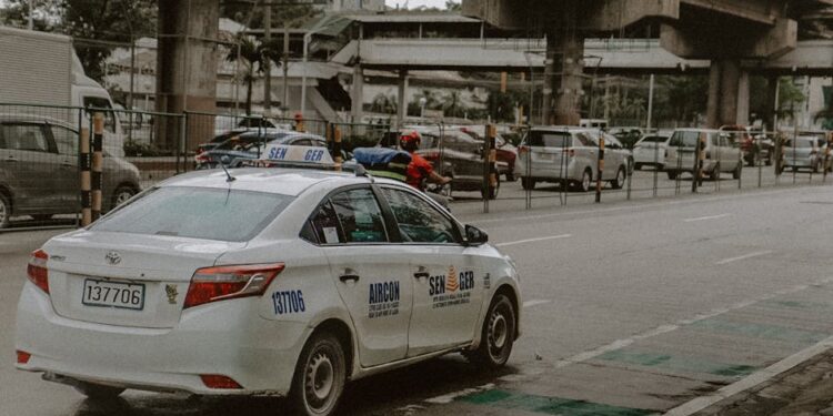 White taxi on a busy street in Quezon City, Philippines, with cars and overpasses in the background.
