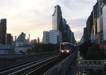 A BTS Skytrain on elevated tracks against the Bangkok skyline during sunset.