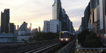 A BTS Skytrain on elevated tracks against the Bangkok skyline during sunset.