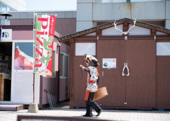 A person in traditional attire walks past a pizza sign in Hokkaido, Japan.