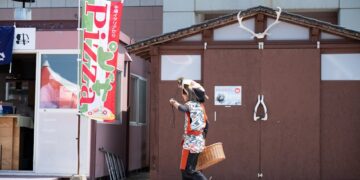 A person in traditional attire walks past a pizza sign in Hokkaido, Japan.