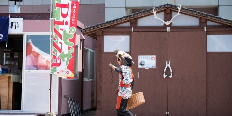 A person in traditional attire walks past a pizza sign in Hokkaido, Japan.