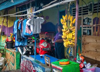Colorful market stall in Banten, Indonesia with bananas, clothes, and a man.