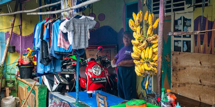 Colorful market stall in Banten, Indonesia with bananas, clothes, and a man.