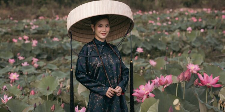 A woman in a traditional Vietnamese outfit stands in a vibrant lotus field, showcasing cultural elegance.