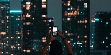 A person photographing Jakarta's illuminated skyscrapers during a vibrant city night.