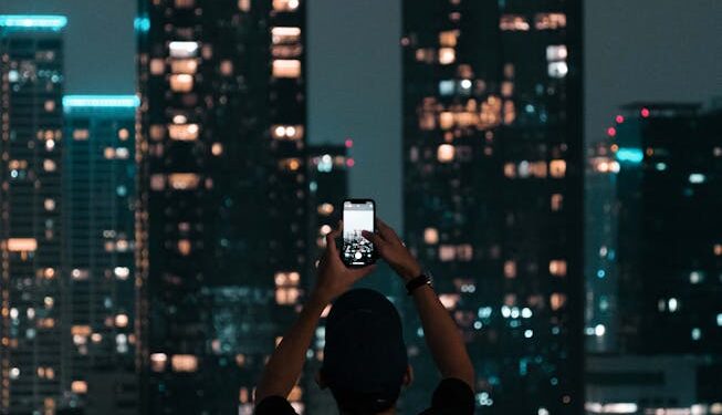 A person photographing Jakarta's illuminated skyscrapers during a vibrant city night.