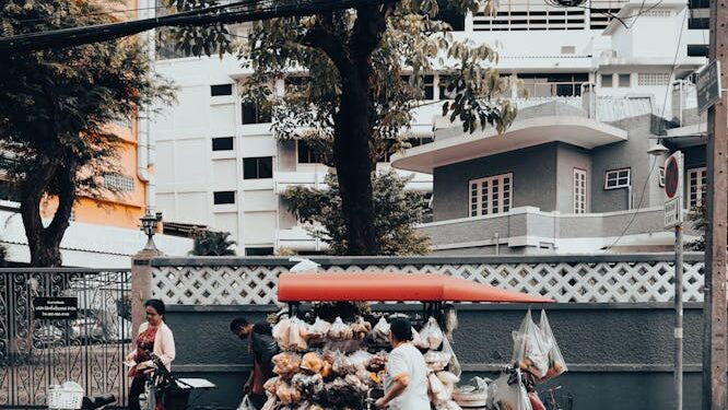 Street vendor with a cart selling goods on a city street in Bangkok, Thailand, showcasing local urban life.